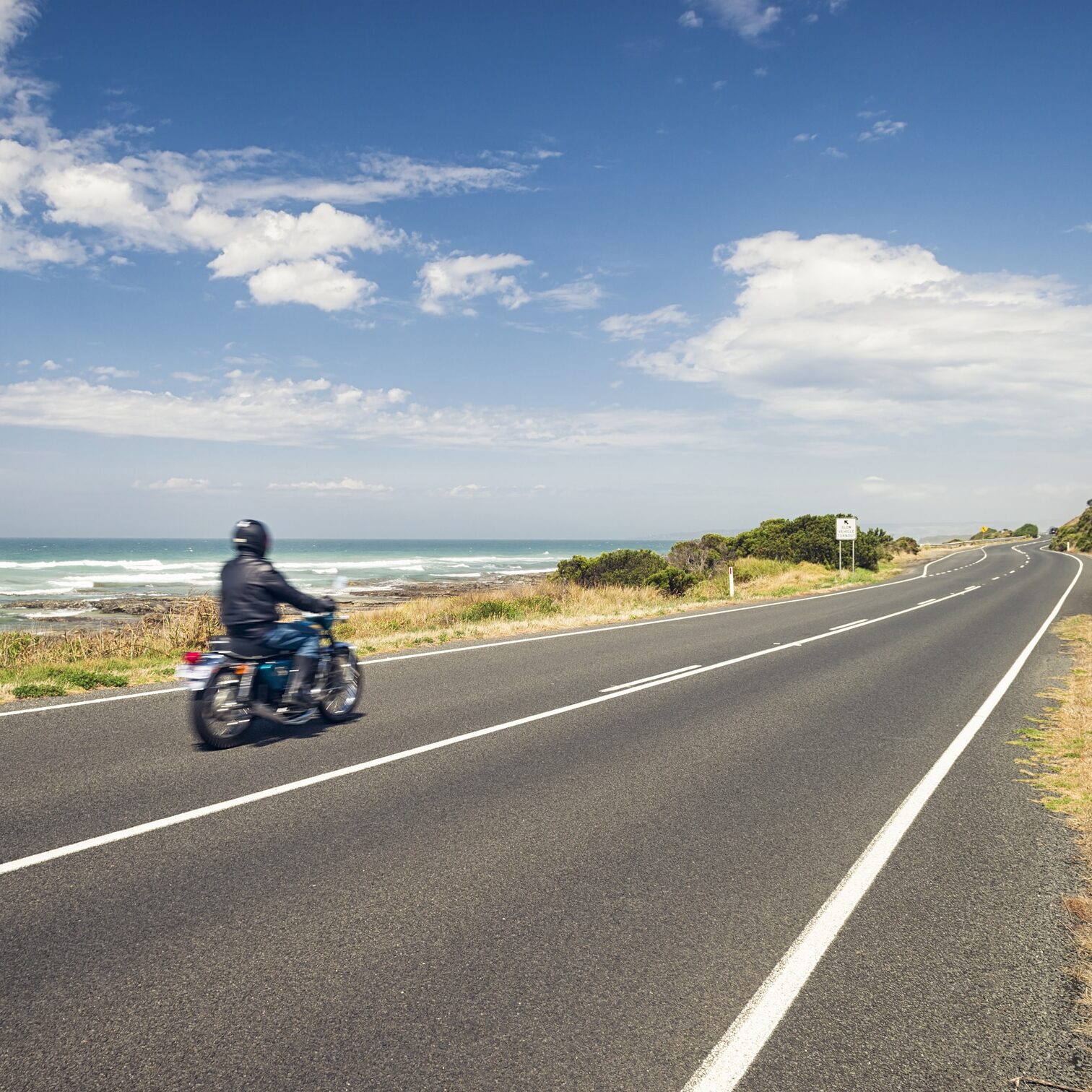 A man riding a motorbike at speed along the Great Ocean Road in Victoria State, Australia. Also known as the Surfcoast Highway, the Great Ocean Road is one of Australia's best known routes.